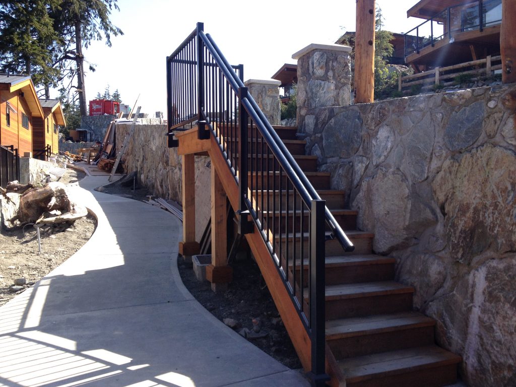 Wood staircase with fascia mount black picket railing and pipe railing for support and building code compliance