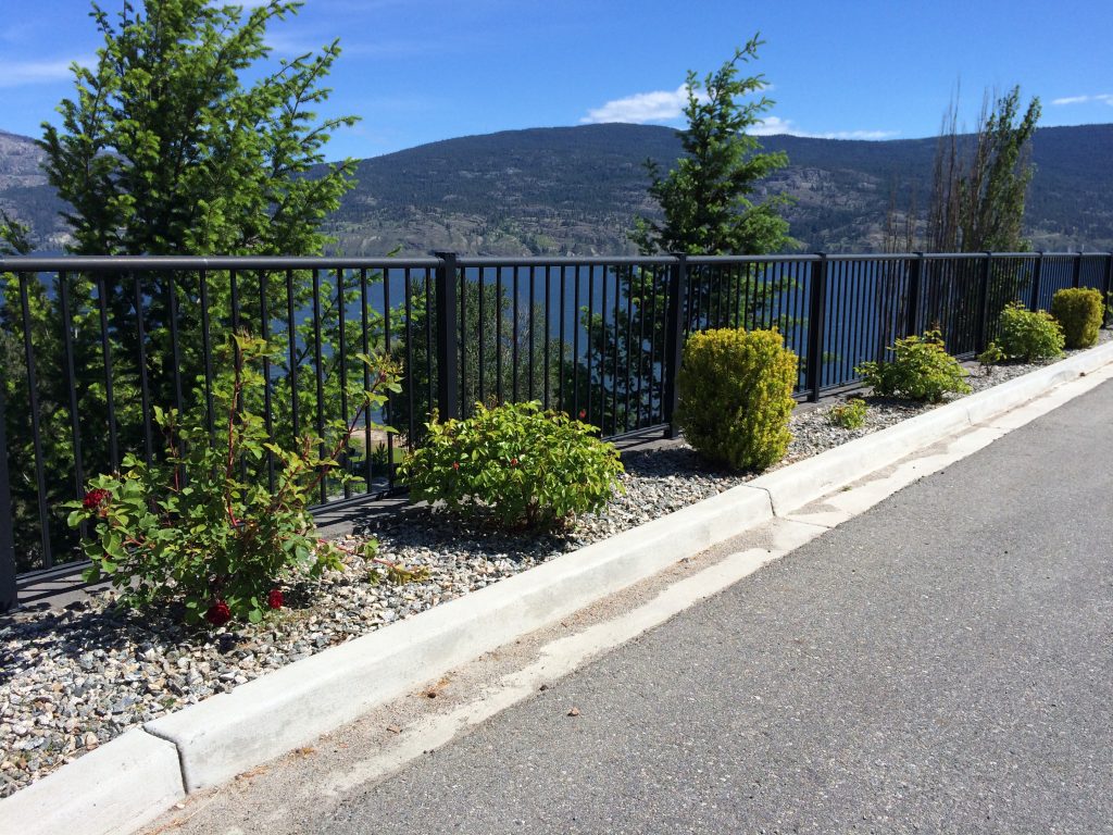 Driveway with commercial landscaping protected by a black picket railing fence